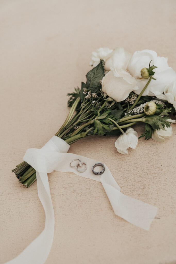 a bouquet of flowers with 3 wedding rings laying on the ribbon