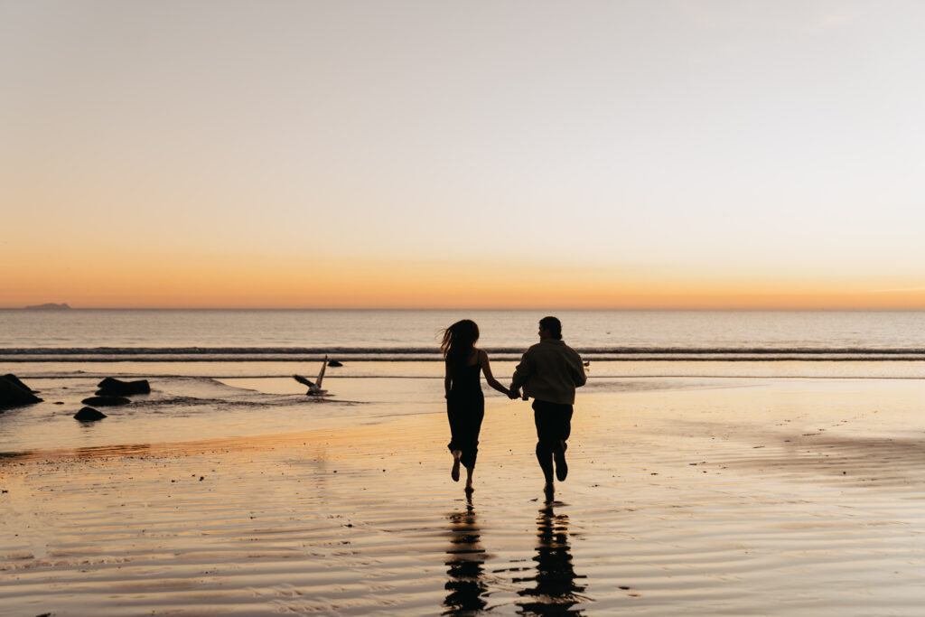 a couple running into the sunset at Coronado beach with a bird flying away 